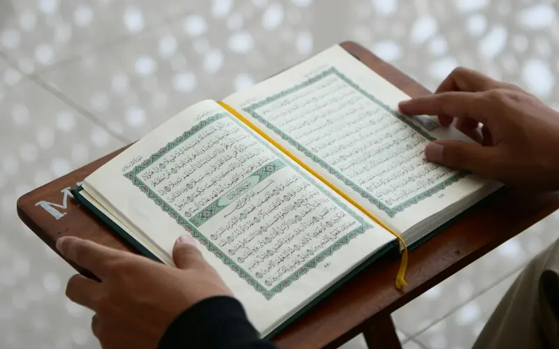 Hands following the text of an open Quran.