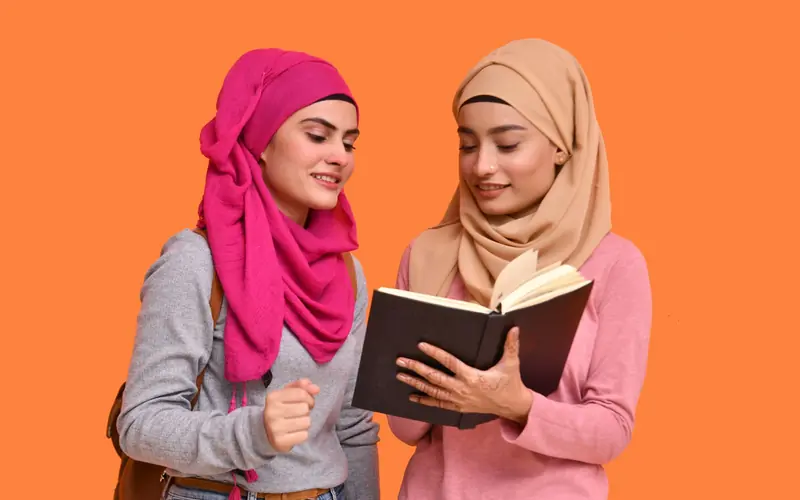 Two women in hijabs reading a book together.